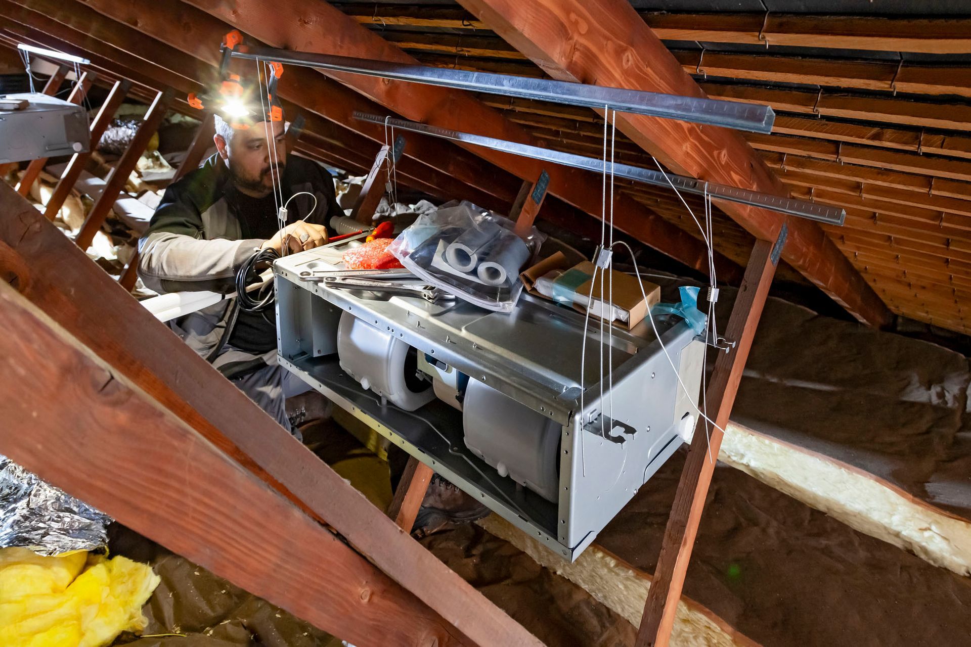 Une personne travaillant sur un système de climatisation suspendu dans un grenier.