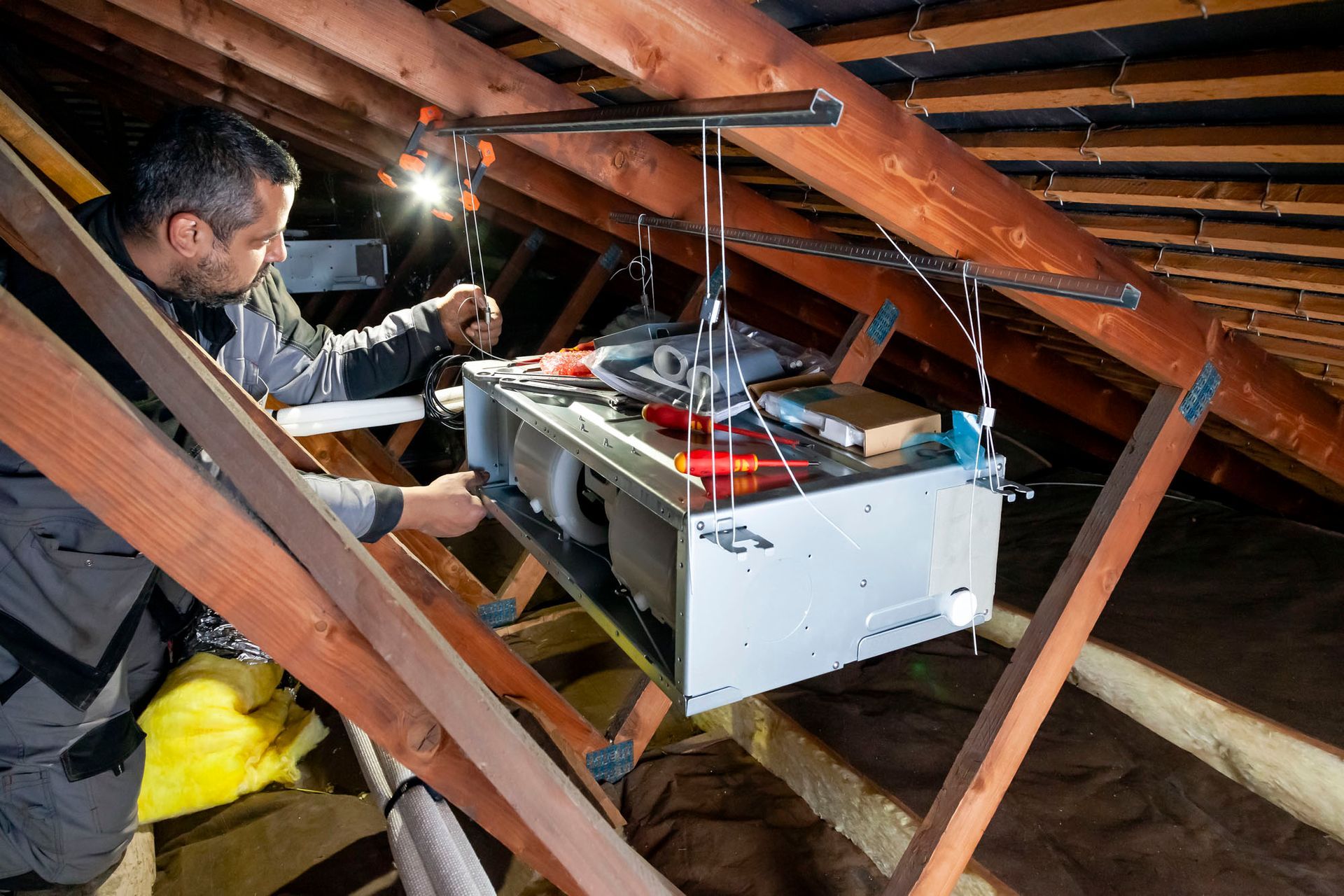Un homme installe un système de climatisation dans un grenier.