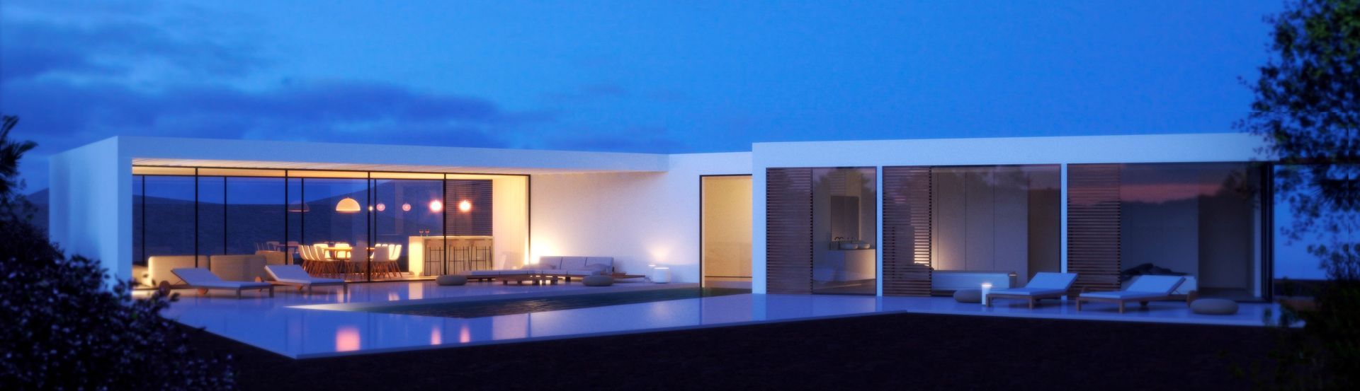 Una casa moderna con grandes paredes de cristal, iluminada desde dentro, con vistas a una piscina al anochecer. El cielo despejado es de un azul intenso.