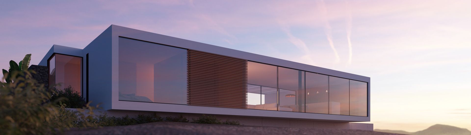 Una casa moderna, rectangular, con paredes de cristal. Se encuentra en una colina con el atardecer de fondo.