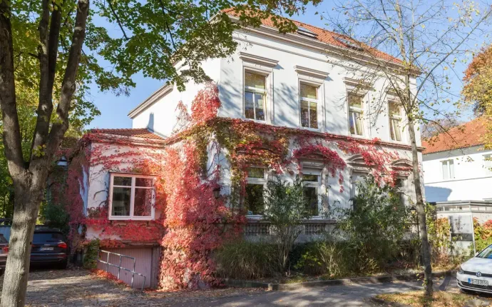 Ein großes weißes Haus einer Kanzlei, an dessen Seite rotes Efeu wächst.