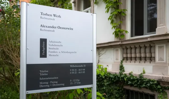 Ein Schild an einem Mast vor einer Kanzlei.