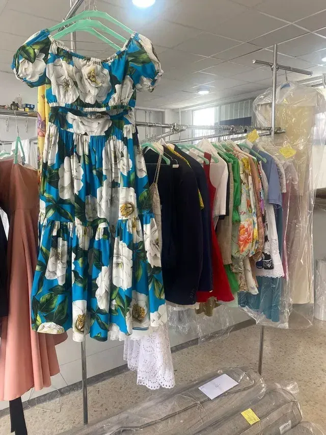 Un vestido azul y blanco con flores colgado en un perchero junto a otras prendas en una tintorería.