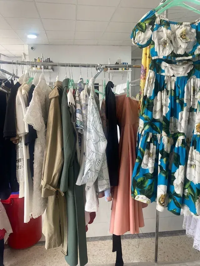 Perchero con varios vestidos y chaquetas en una tienda. Incluye un vestido azul floral.