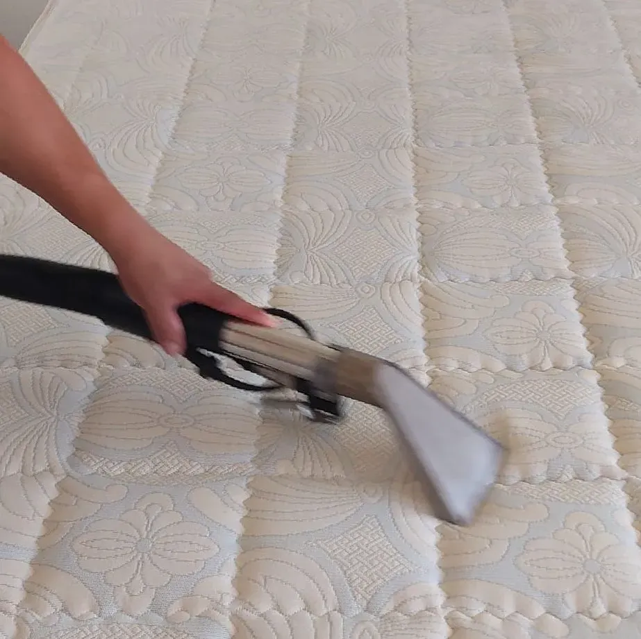 Una persona está limpiando un colchón con una aspiradora.
