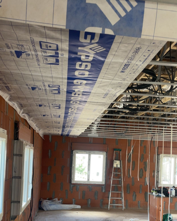 Intérieur d'une pièce en construction avec isolation au plafond et murs et fenêtres en briques apparentes.