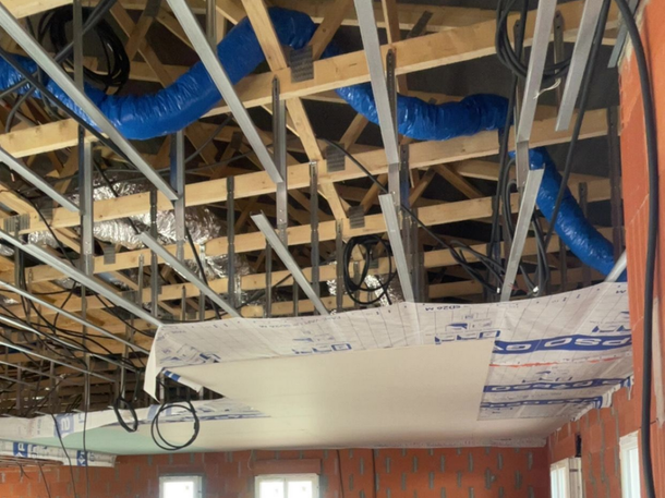 Charpente et conduits de plafond apparents dans un bâtiment en construction, avec des conduits et des câbles de climatisation bleus visibles.