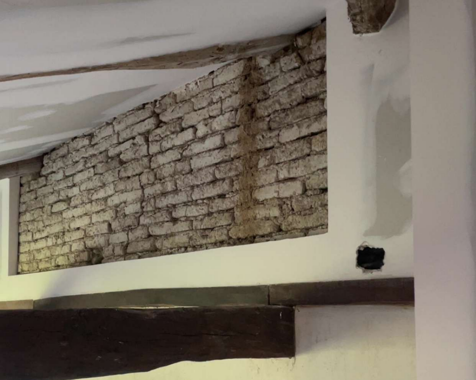 Mur intérieur en briques apparentes, plâtre blanc et poutres en bois foncé près du plafond.