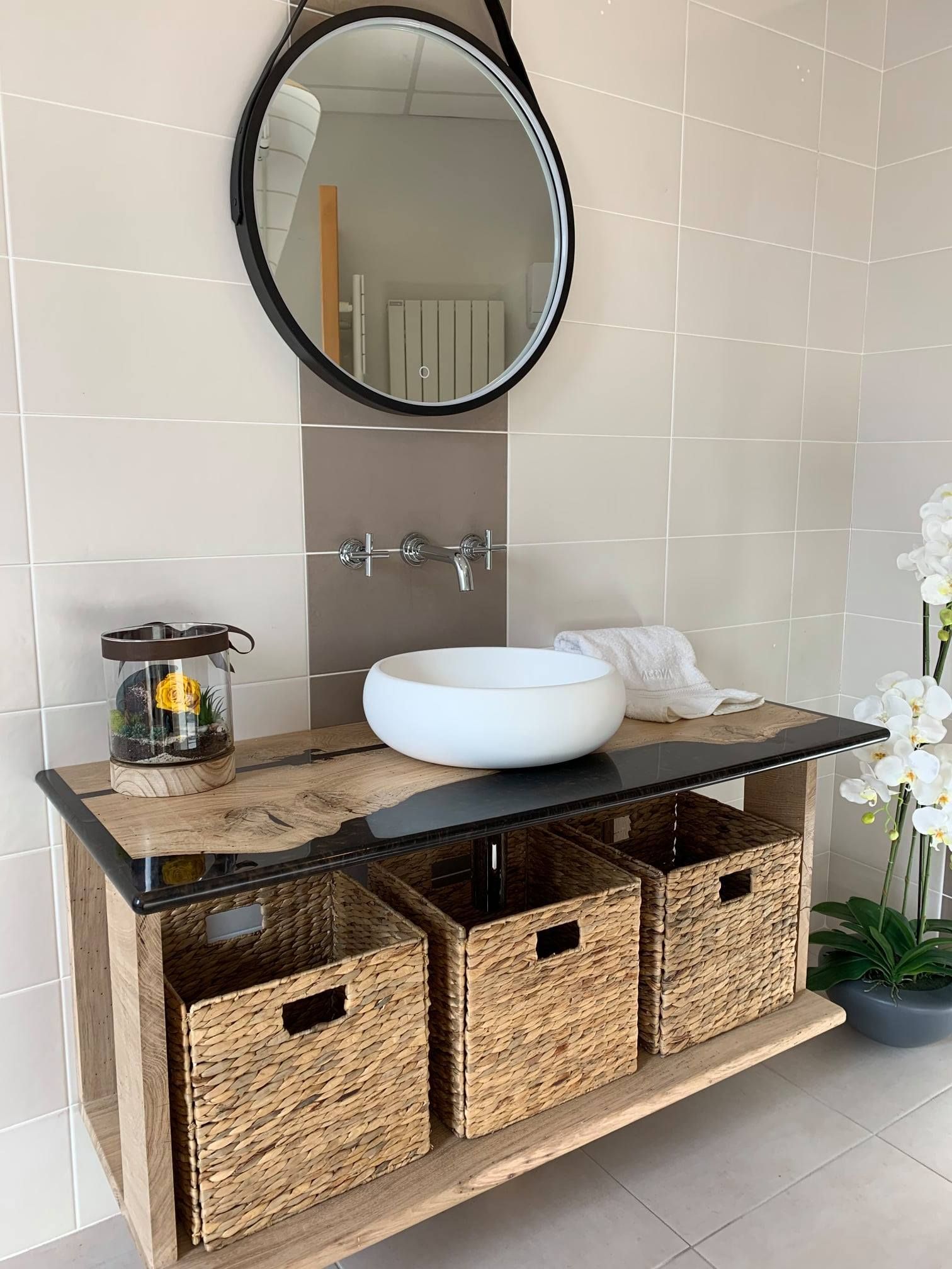 Meuble-lavabo moderne avec miroir rond, vasque blanche, paniers tressés et objets décoratifs sur une table en bois