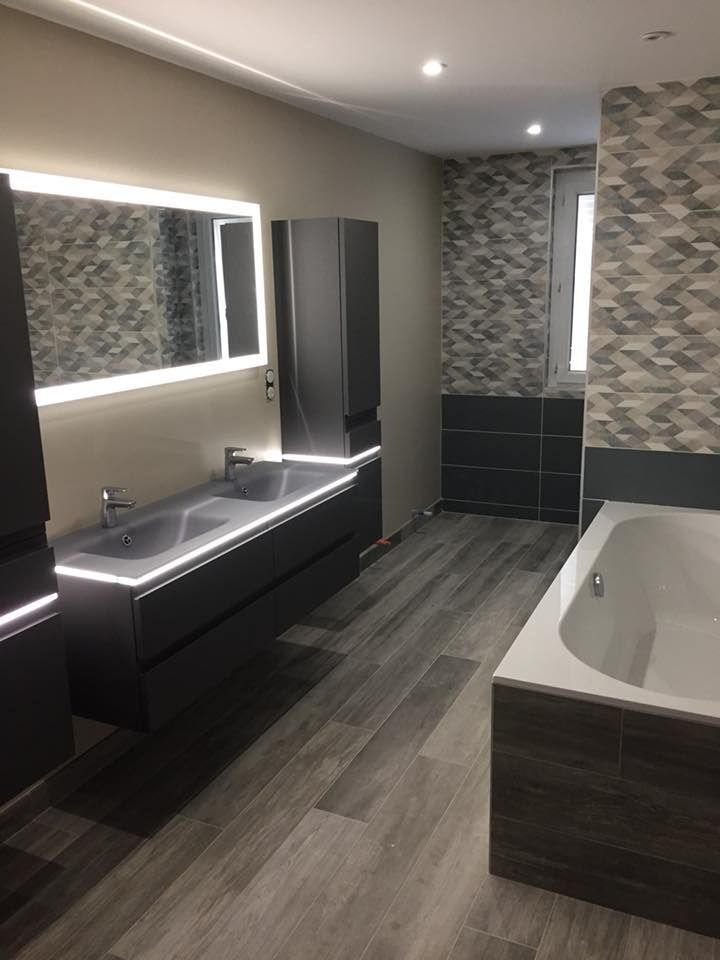 Salle de bains moderne avec double vasque, miroir éclairé, murs carrelés et baignoire îlot.