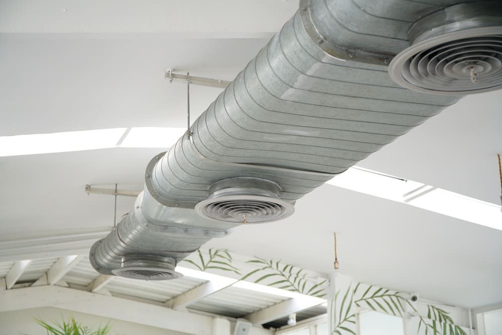 Plafond avec de grands conduits de ventilation argentés et des grilles d'aération circulaires dans un espace intérieur lumineux