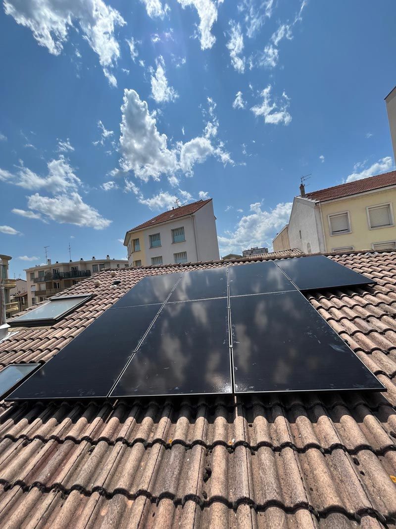 Des panneaux solaires installés sur un toit de tuiles en terre cuite sous un ciel bleu partiellement nuageux.