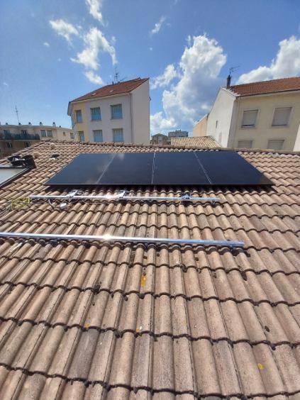 Des panneaux solaires installés sur un toit de tuiles en terre cuite sous un ciel bleu parsemé de nuages