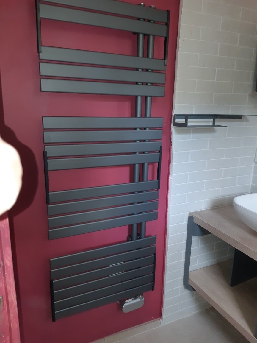 Radiateur sèche-serviettes noir moderne sur un mur rouge dans une salle de bains avec lavabo blanc