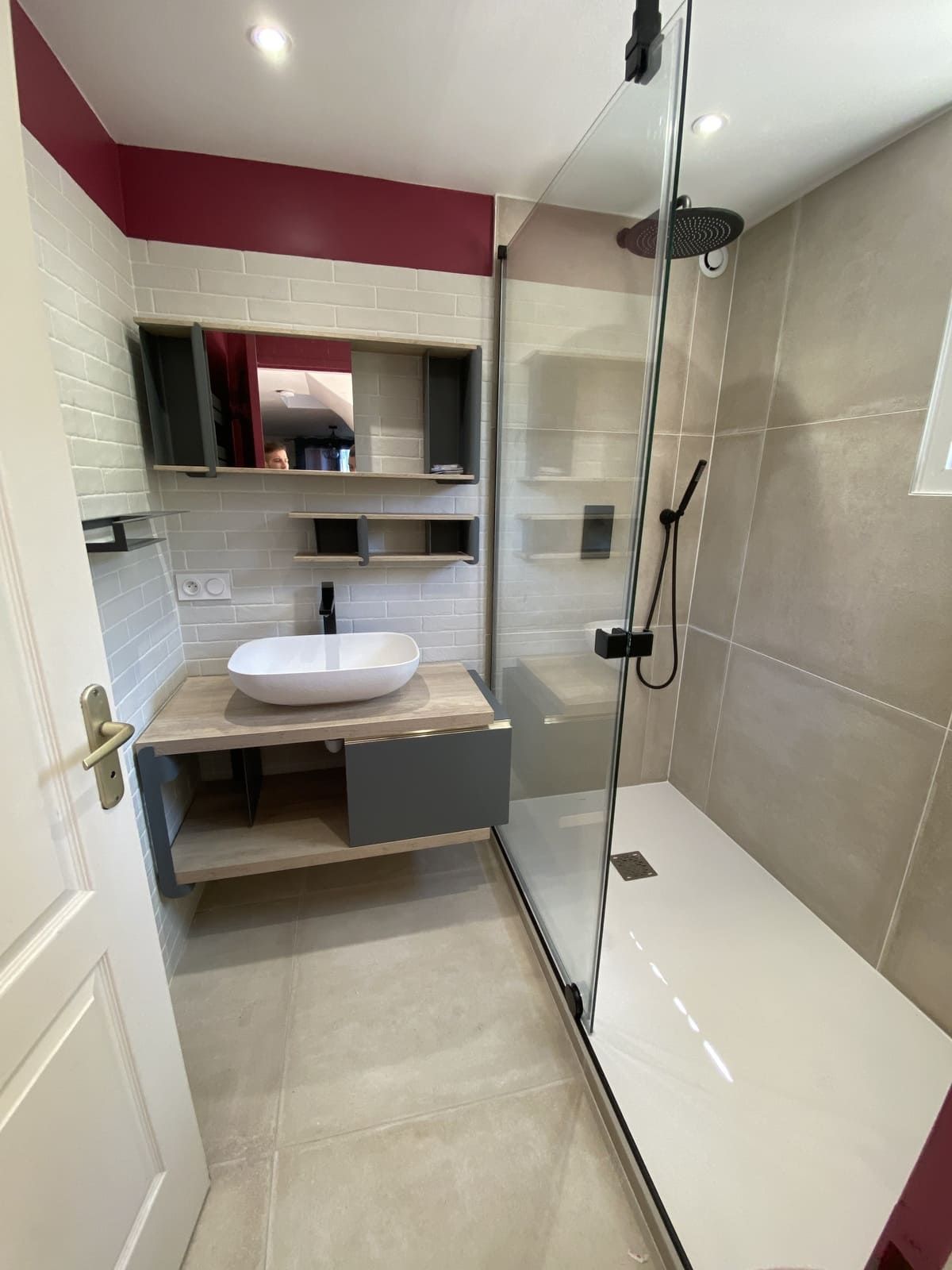 Salle de bain compacte avec carrelage beige, meuble vasque blanc, étagères à miroir et cabine de douche en verre