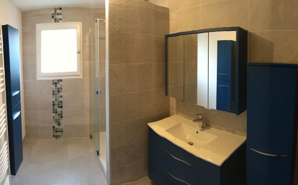 Salle de bains moderne avec douche, lavabo, armoire de toilette et meubles bleus.