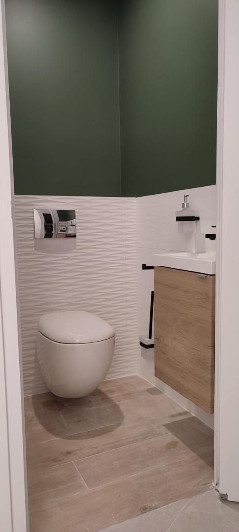 Salle de bain moderne avec toilettes, lavabo, murs verts et meuble-lavabo en bois