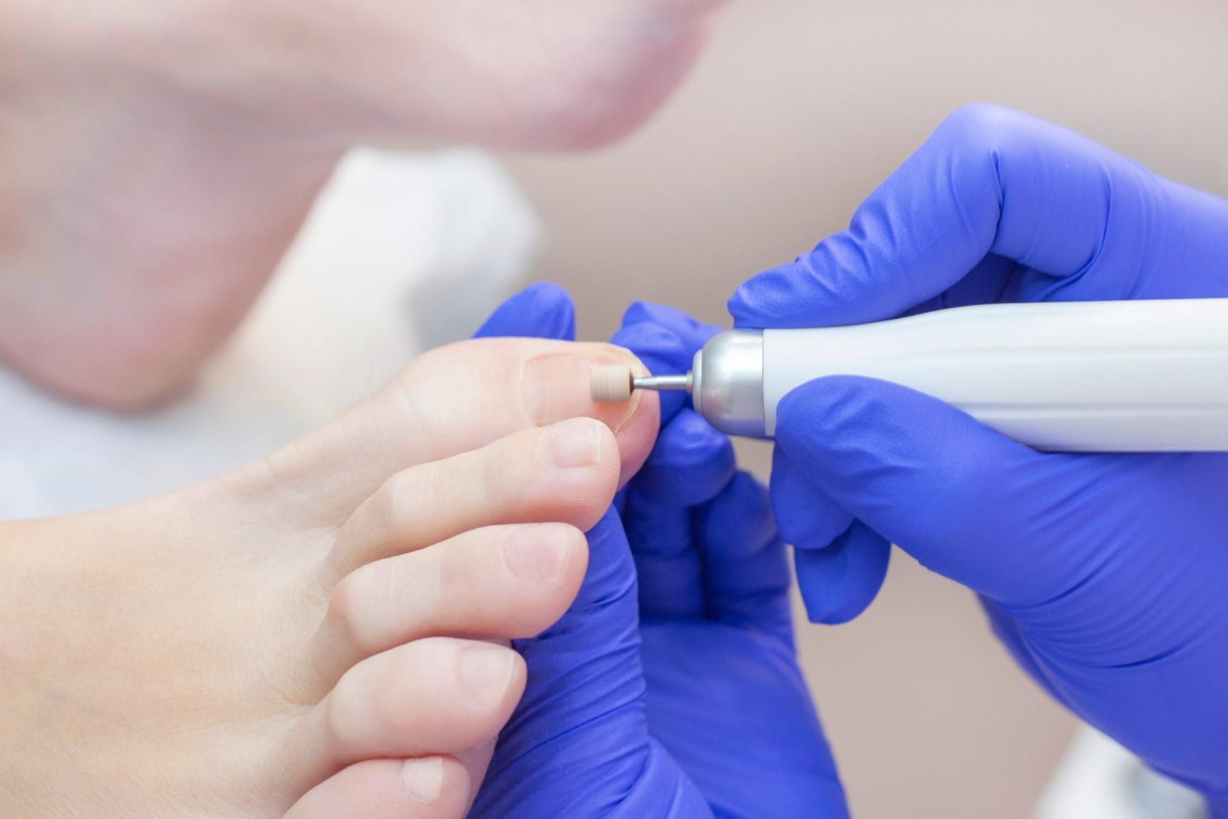 Manos enguantadas usando un torno de uñas en la uña de una persona en un salón de belleza (primer plano)
