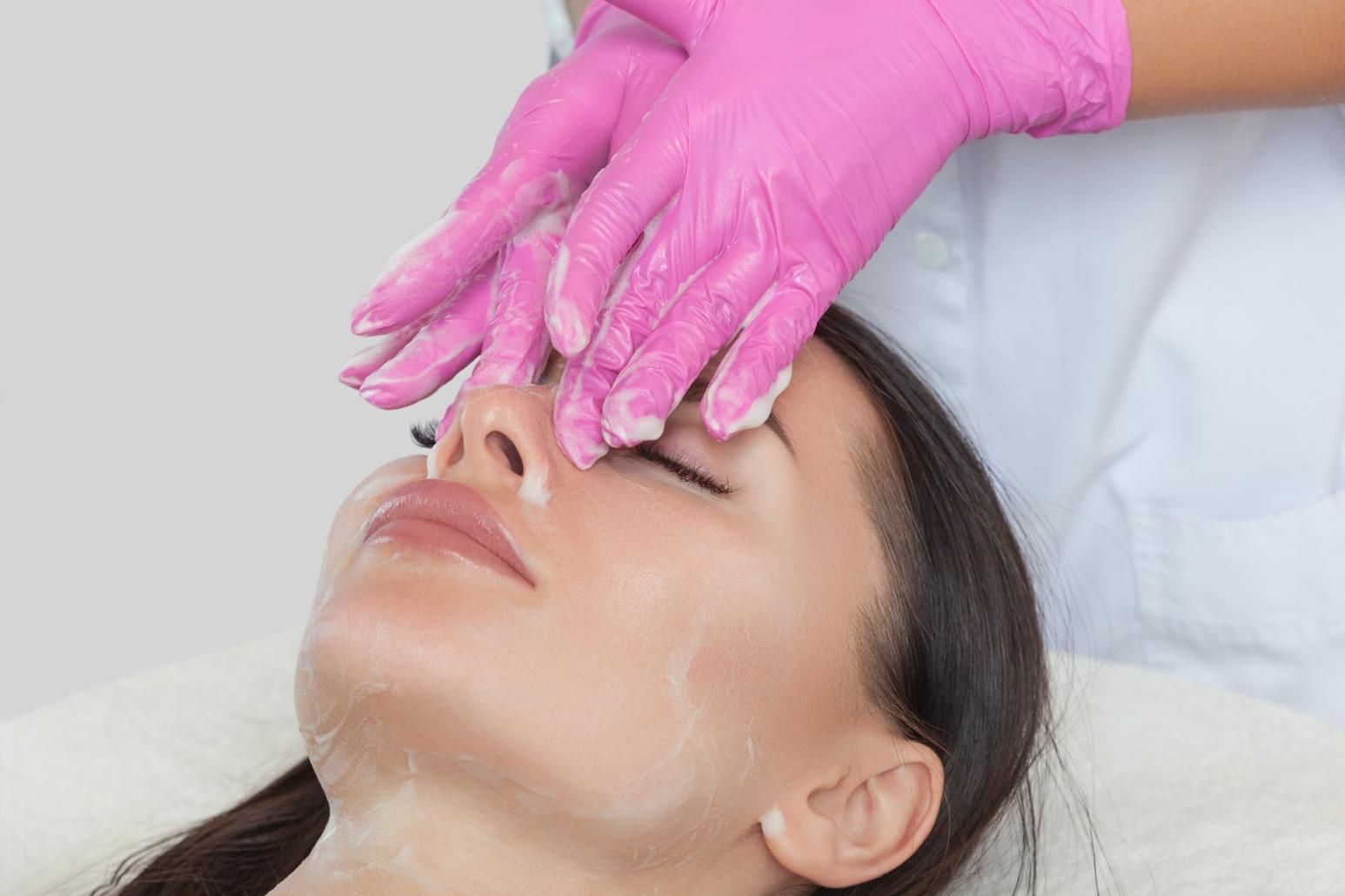 Unas manos enguantadas aplican un tratamiento facial a una persona recostada en un entorno de spa.