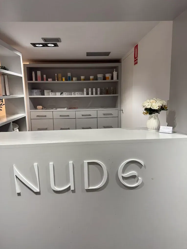 Mostrador de recepción minimalista para salón de belleza con letrero NUD6, estantes con productos y flores blancas.