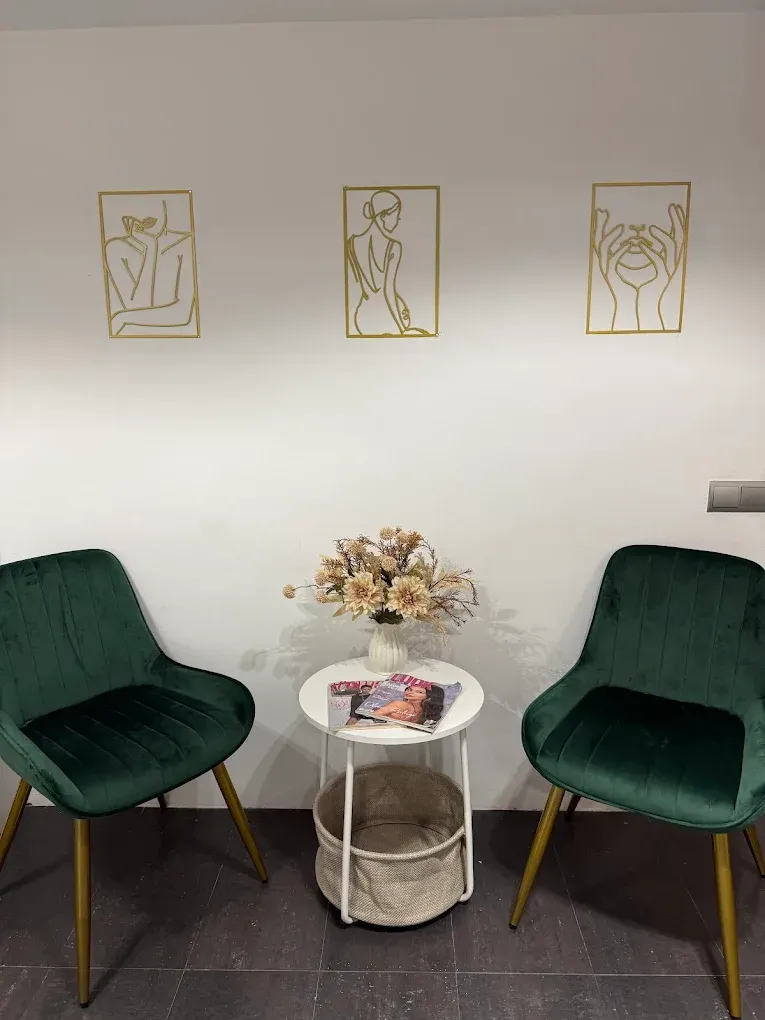 Zona de espera con dos sillas verdes, una pequeña mesa redonda con flores y revistas