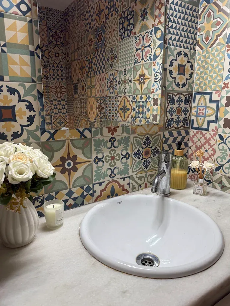 Lavabo decorativo con salpicadero de azulejos estampados, flores y pequeñas velas sobre la encimera.