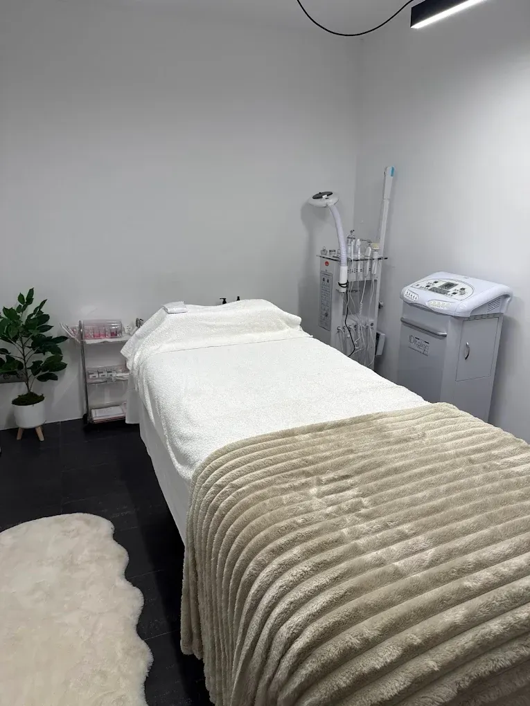 Sala de tratamientos de spa con camilla de masaje, sábanas blancas, manta beige y equipo para el cuidado de la piel.