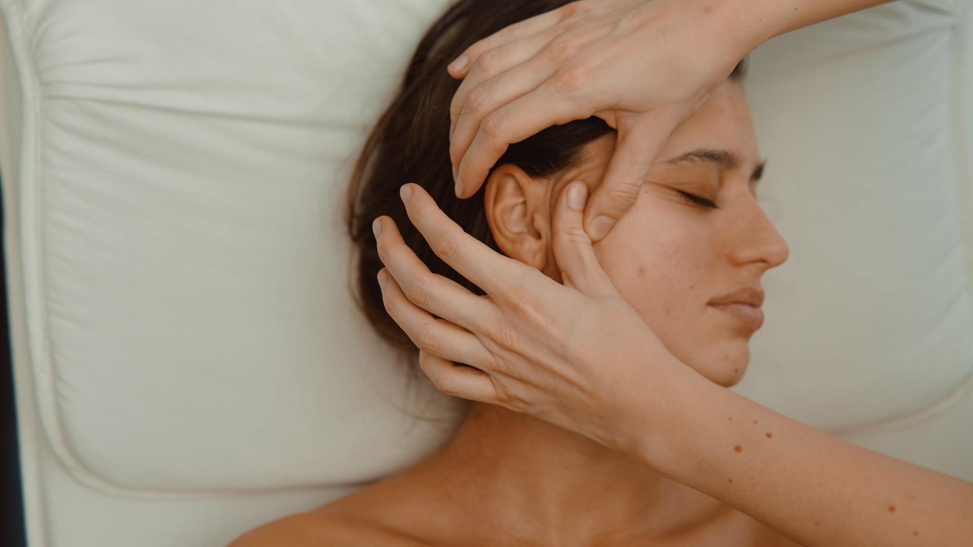 Mujer recibiendo un suave masaje facial mientras está tumbada sobre una almohada blanca.