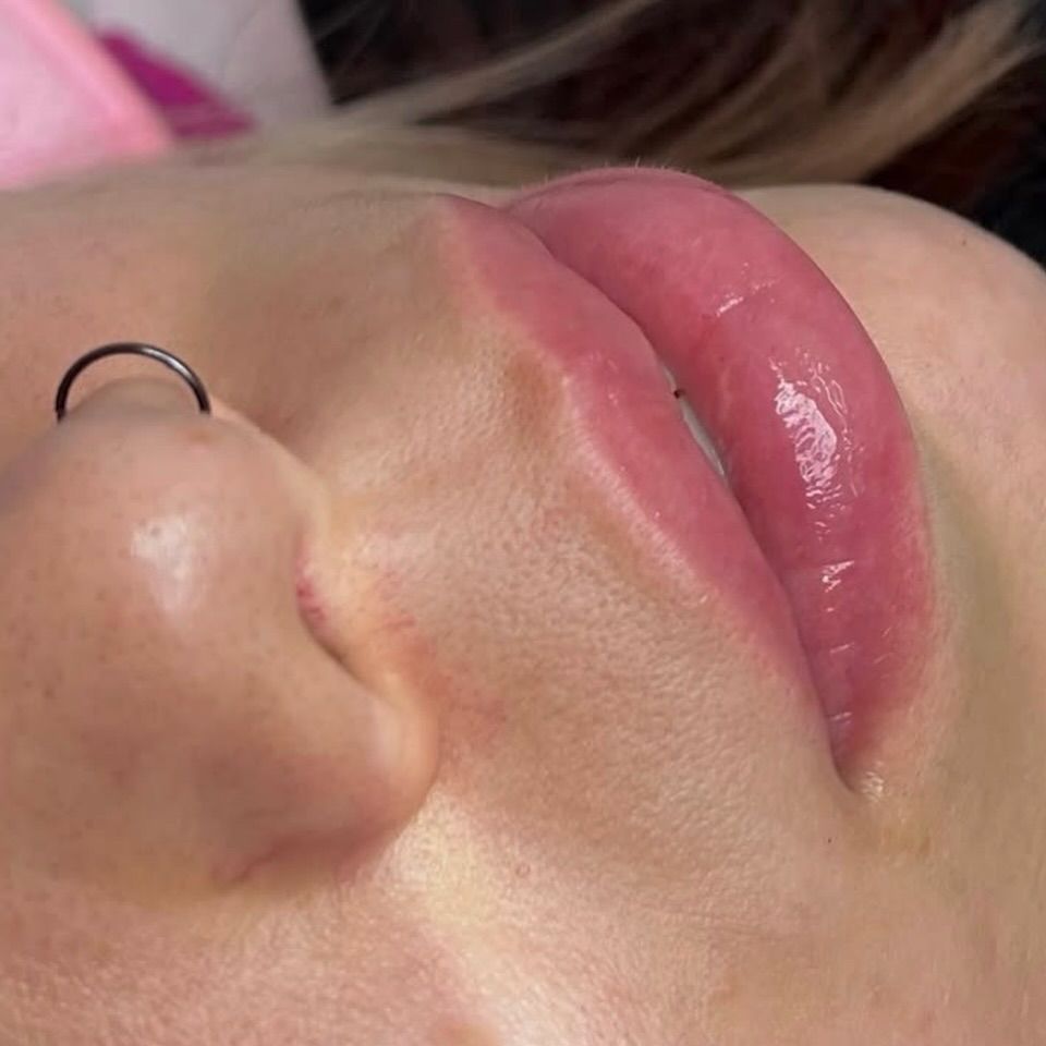 Primer plano del rostro de una persona con labios rosados ​​brillantes y un pequeño aro en la nariz.