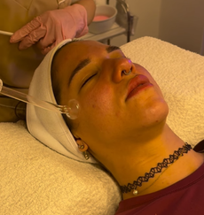 Persona recibiendo un tratamiento facial mientras está recostada con una diadema y una mano enguantada aplicándole cuidados.