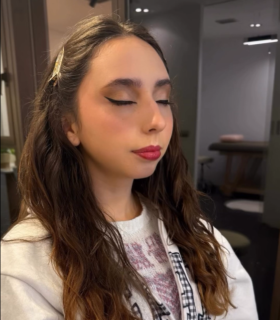 Mujer en el interior de una habitación con los ojos cerrados, vestida con una blusa blanca y lápiz labial rosa