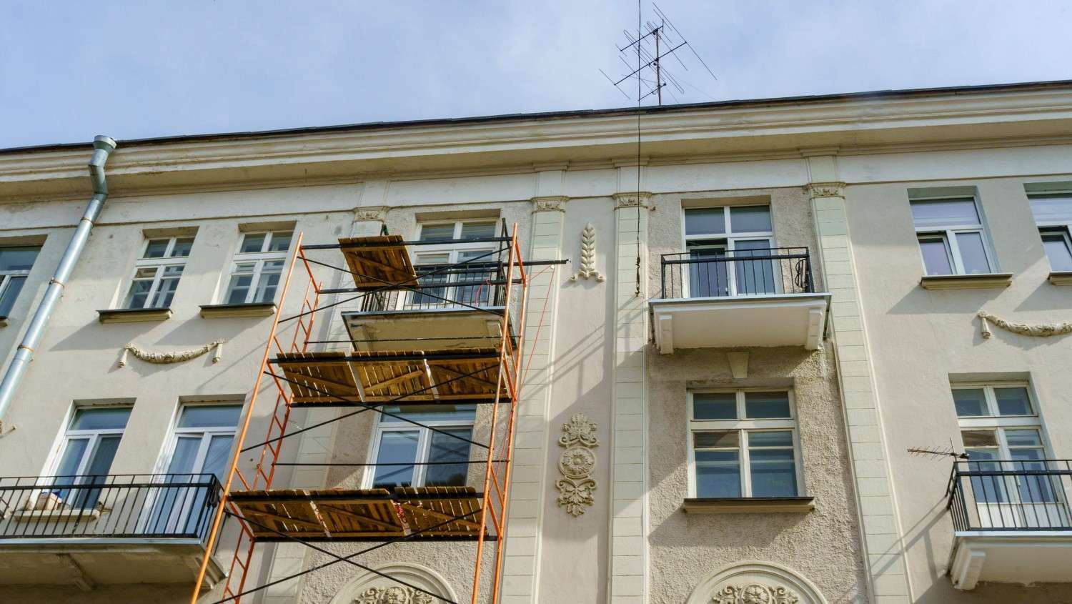 Andamios contra un edificio color crema. Se ven ventanas, balcones y una antena.