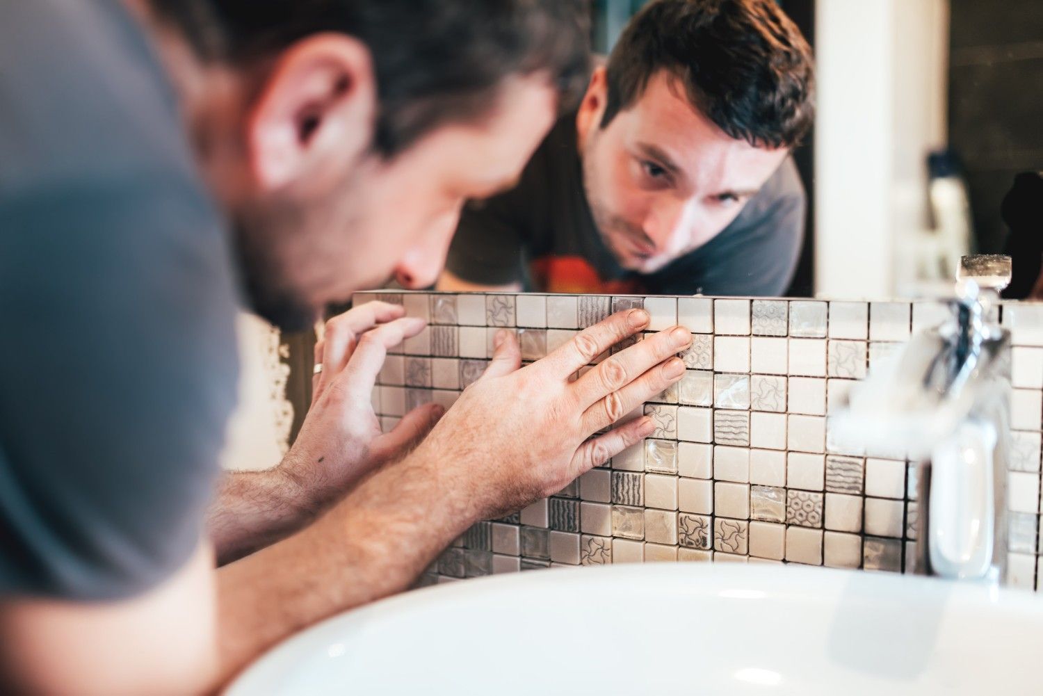 Hombre instalando protector contra salpicaduras de azulejos en el baño, concentrado en el trabajo.
