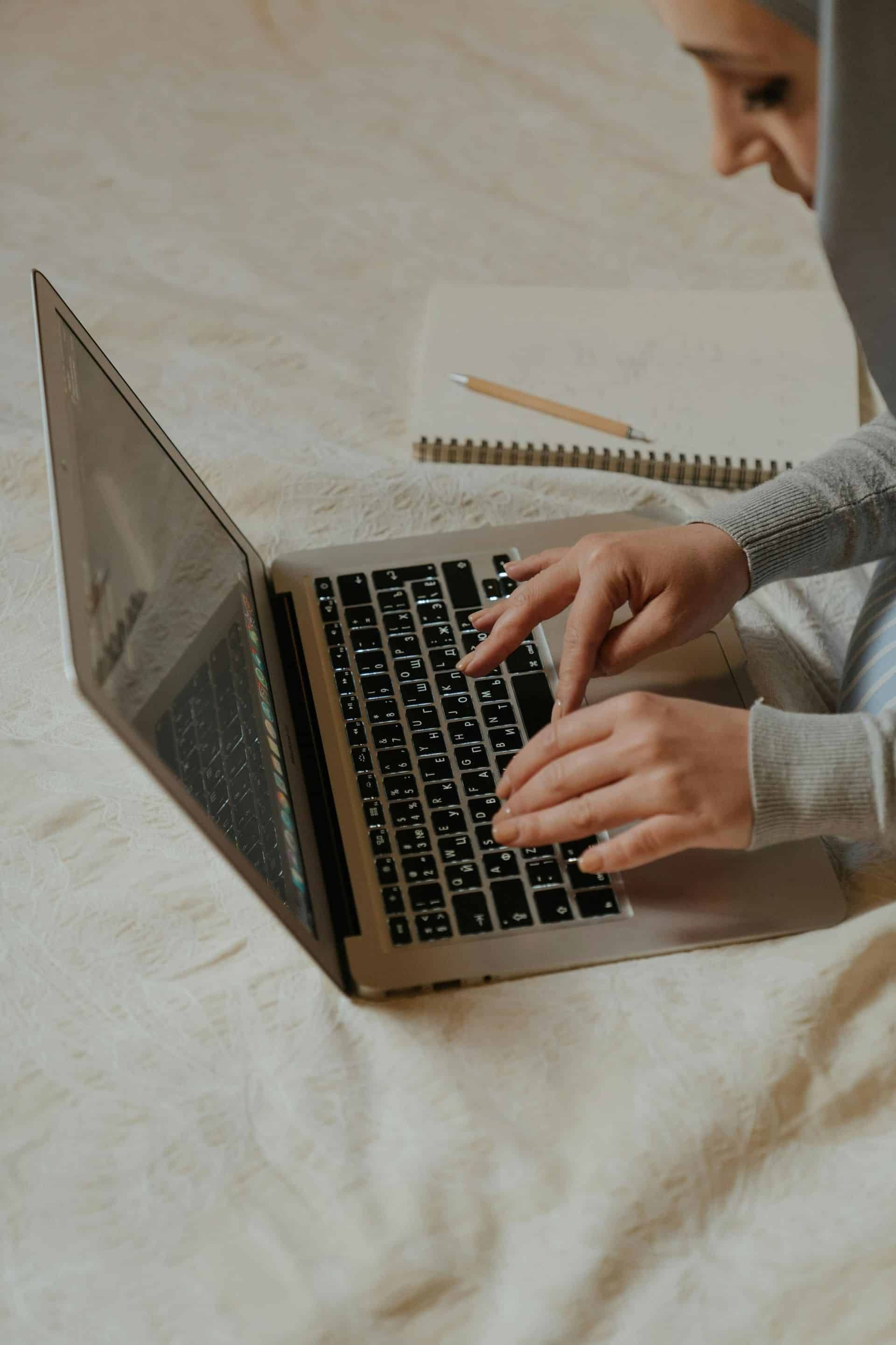 Eine Frau sitzt auf einem Bett und benutzt einen Laptop.
