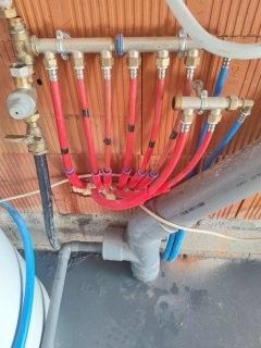 Système de tuyauterie avec des tuyaux rouges et bleus raccordés à des collecteurs en laiton, contre un mur de briques.