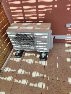 Unité de climatisation sur un sol carrelé, projetant des ombres, contre un mur.