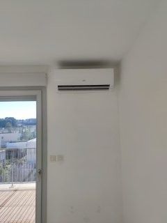 Climatiseur blanc fixé sur un mur blanc. À côté d'une porte vitrée donnant sur l'extérieur.