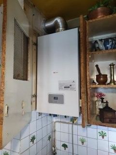 Chaudière murale blanche dans une cuisine, avec conduit d'évacuation, tuyaux et murs carrelés.