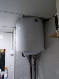 Un chauffe-eau blanc fixé au mur d'une salle de bains, avec les tuyaux visibles en dessous.