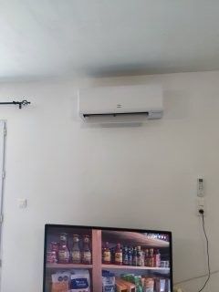 Unité de climatisation blanche sur un mur blanc au-dessus d'un téléviseur présentant une vitrine de marchandises.