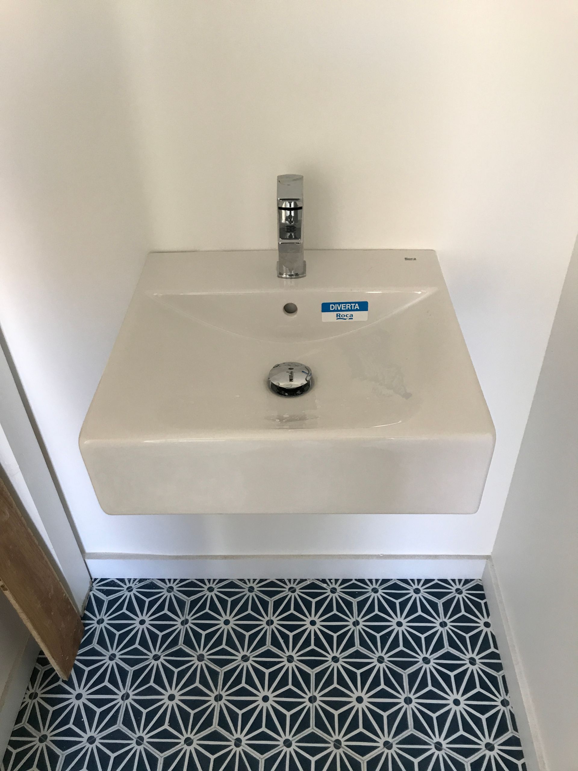 Lavabo carré blanc avec robinet chromé, au-dessus d'un carrelage bleu et blanc à motifs.