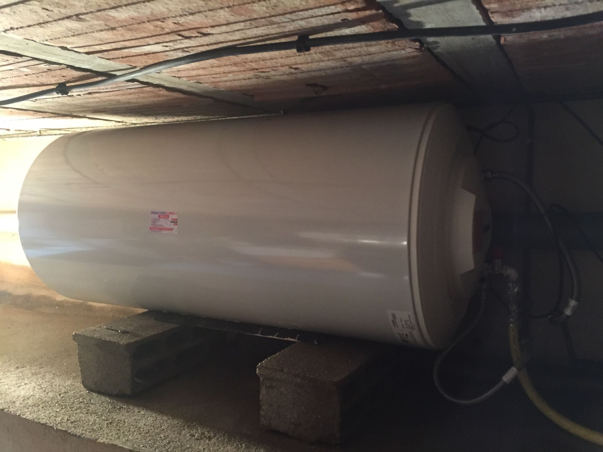 Chauffe-eau blanc posé sur des blocs de béton sous un plafond en briques.