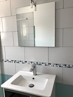 Salle de bains avec lavabo blanc, miroir et murs carrelés.