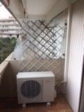 Unité de climatisation sur un balcon, devant une treille.
