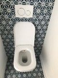 Toilettes blanches avec abattant ouvert, contre un mur recouvert de carreaux à motifs géométriques bleus et blancs.