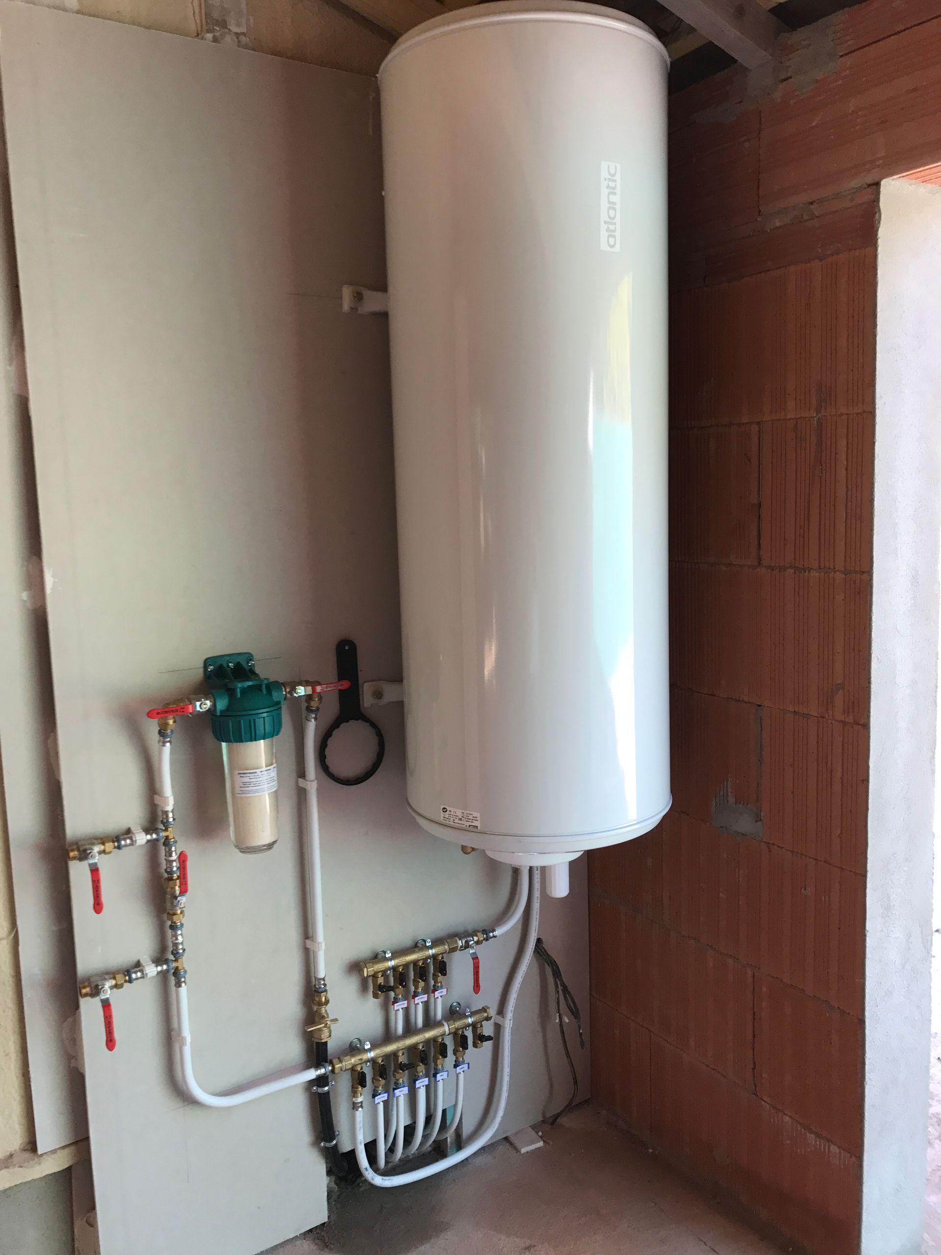 Chauffe-eau blanc fixé sur un mur carrelé de salle de bain.