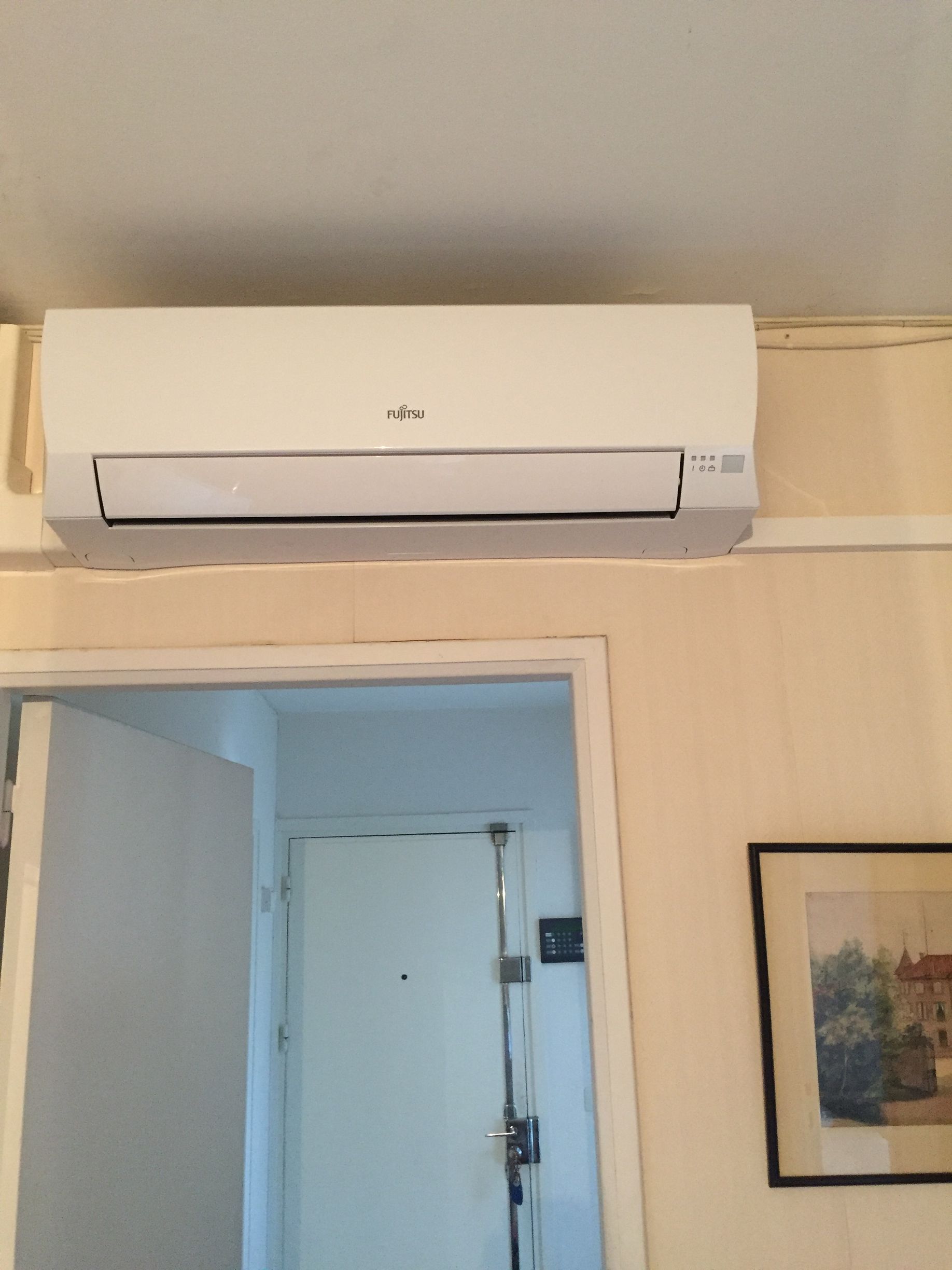 Climatiseur blanc installé au-dessus d'une porte dans une pièce aux murs clairs.