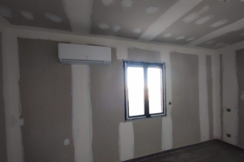 Pièce intérieure avec cloisons sèches, fenêtre et climatiseur.