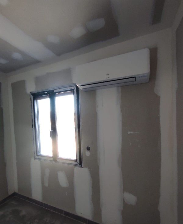 Une pièce inachevée avec une fenêtre, un climatiseur et des cloisons sèches partiellement installées.