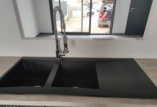 Évier de cuisine noir avec robinet flexible, devant une fenêtre.